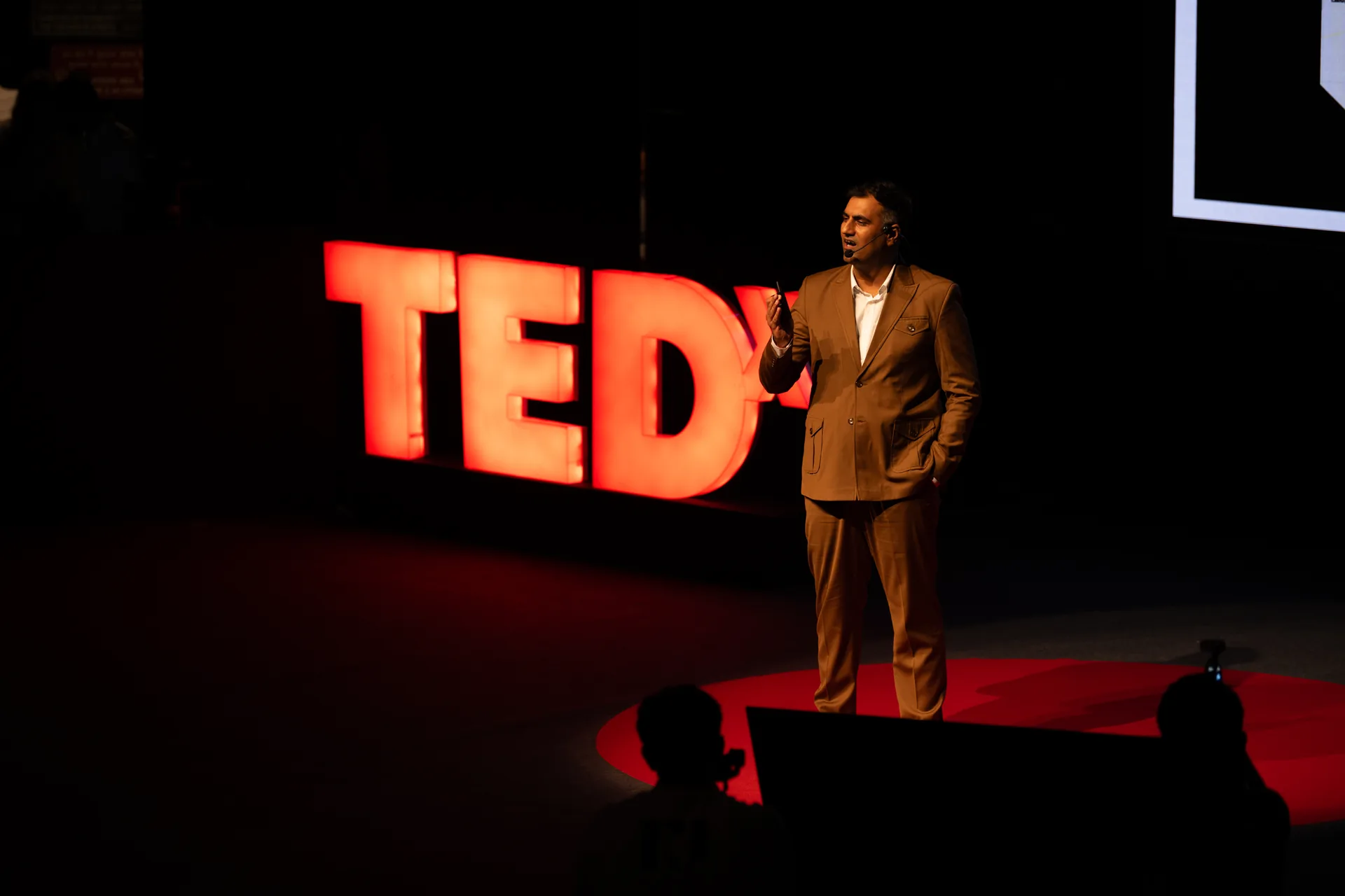 Ar. Vishwas Chadha speaking beside the illuminated TEDx letters at TEDx Sukhna Lake